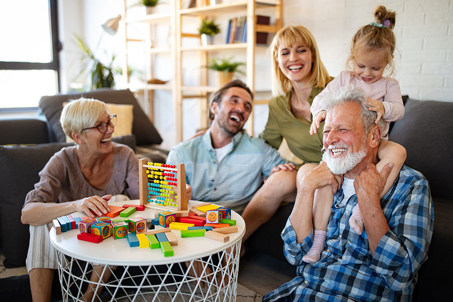 Personal Insurance - Grandparents, Parents and a Small Girl are Laughing Together and Playing With Blocks While the Small Girl is Sitting on Her Grandfather's Shoulders at Home